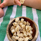 Wooden bowl of 16 oz 1-3-5 American Sign Language Handshaped Pasta. Child holding a pasta piece on green striped cloth