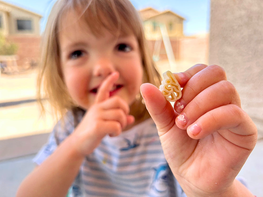 Toddler holding a piece of 16 oz 1-3-5 American Sign Language Handshaped Pasta. Close up showing playful mealtime moment